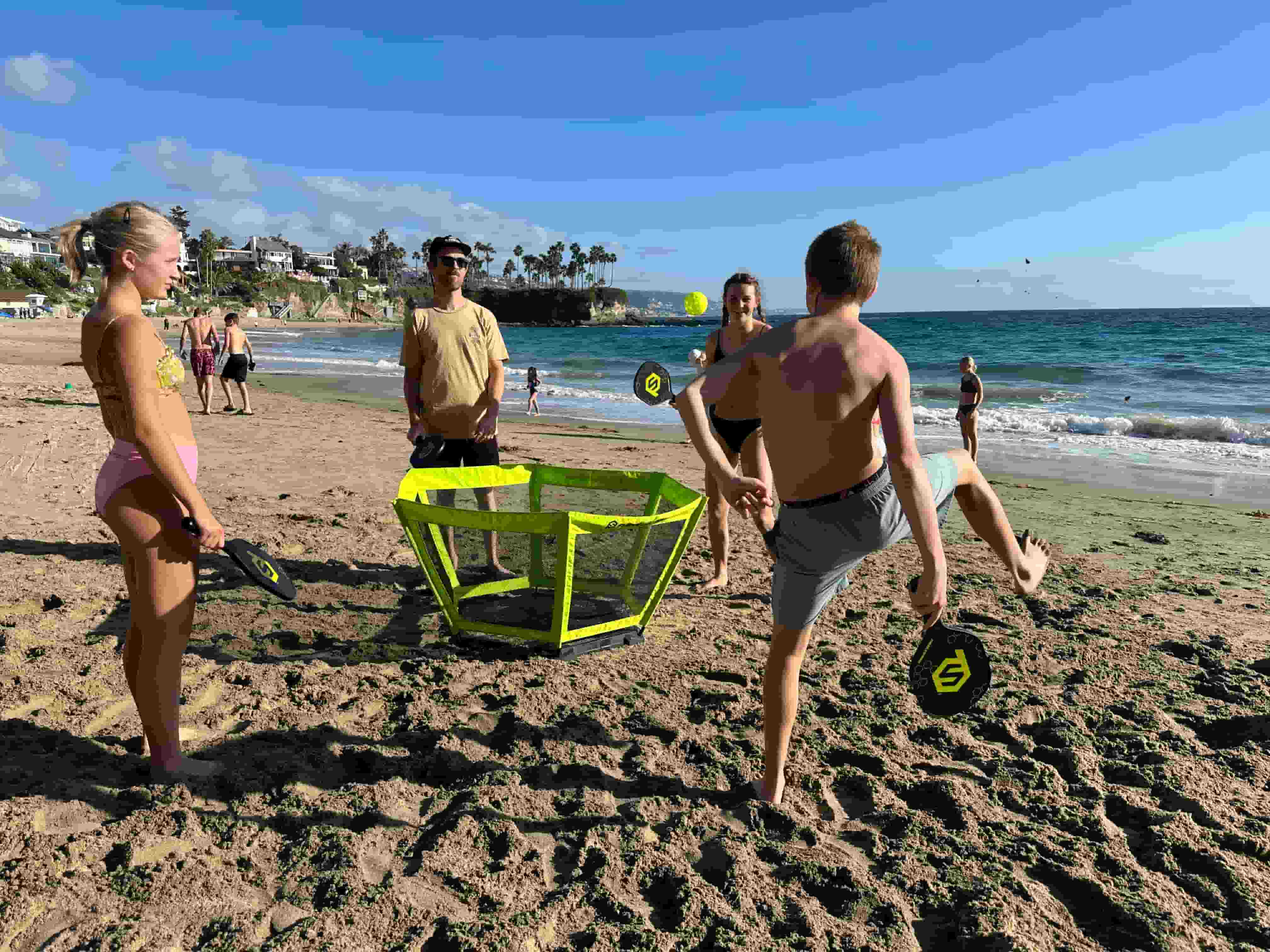 : A family playing at the beach, its a sunny day, the guy is performing a trick