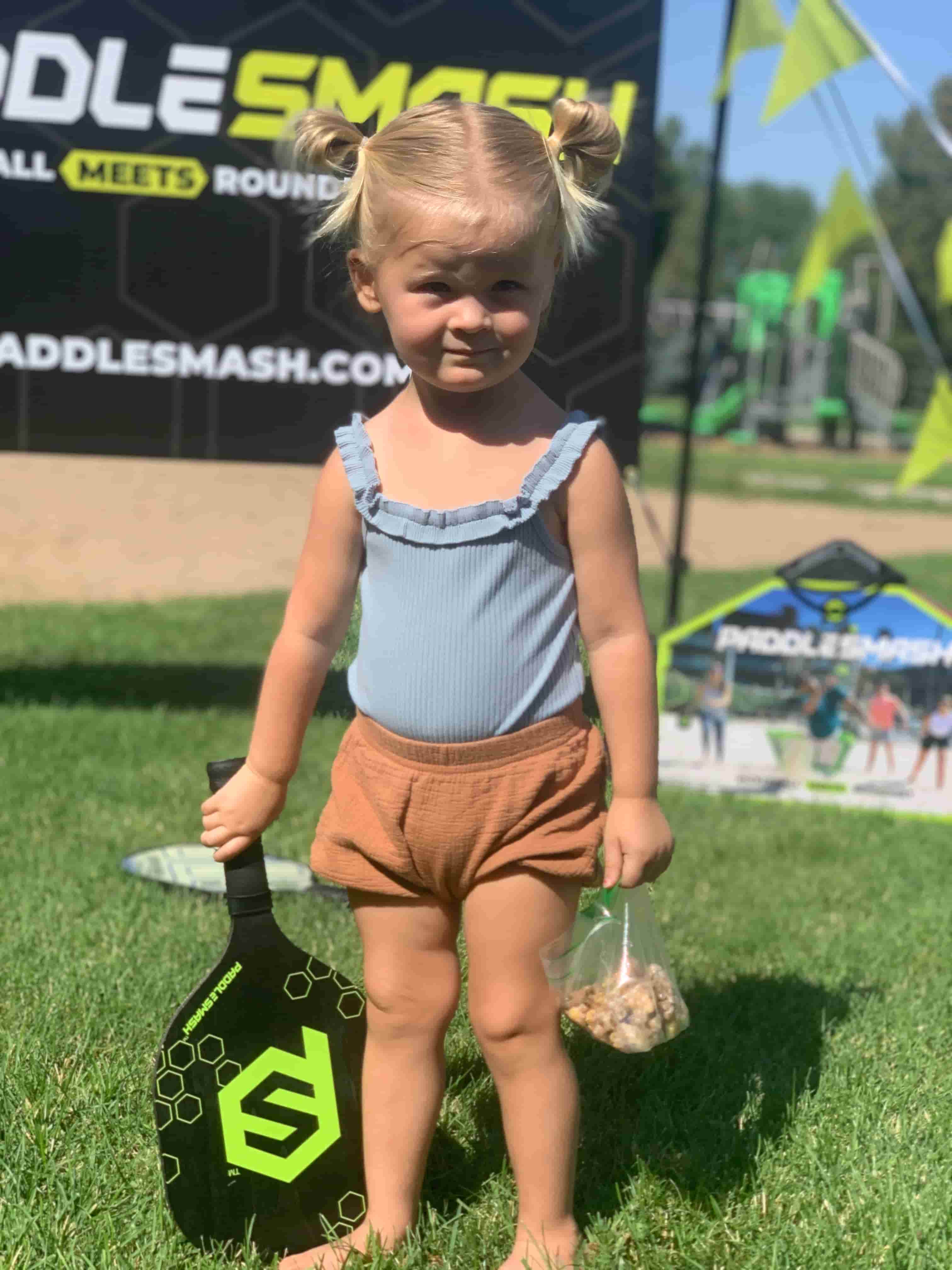 Toddler girl is holding a PaddleSmash paddle on a sunny day