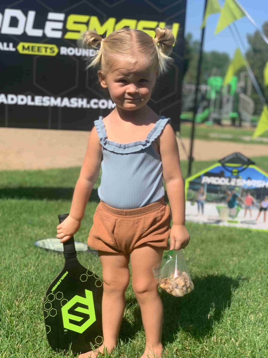 Toddler girl is holding a PaddleSmash paddle on a sunny day