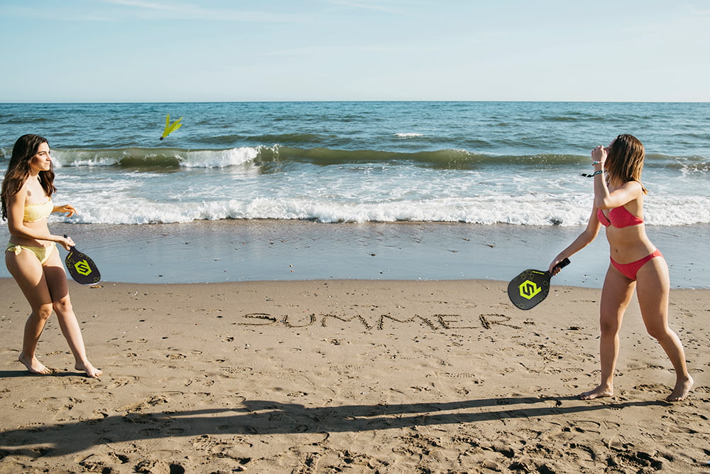Two girls holding PaddleSmash paddles at the beach, playing with smashbirdies
