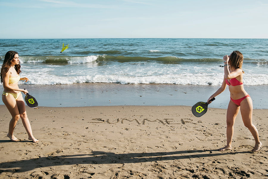 Two girls holding PaddleSmash paddles at the beach, playing with smashbirdies